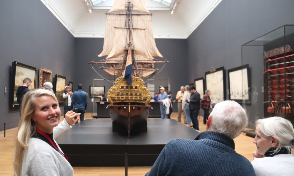 People looking at a model ship on display. The model appears to be of a historical sailing vessel.