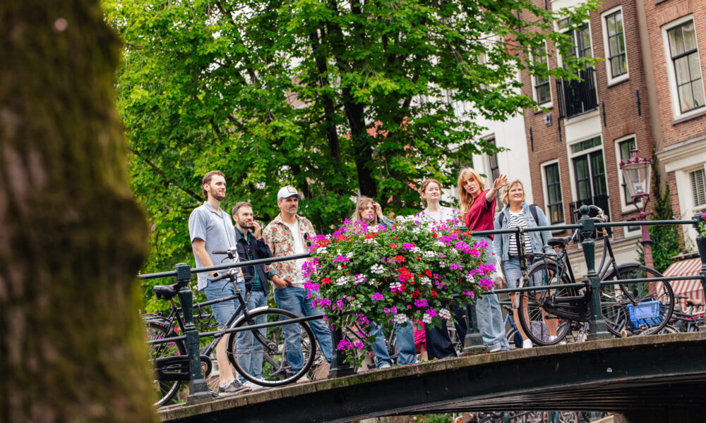 Group of people on a bridge with flowers in Amsterdam. The bridge has a metal railing and bicycles are parked on it.