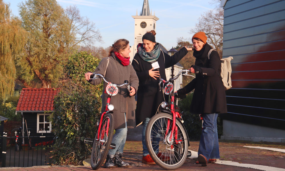 Three women with red bikes on a street. They look happy.