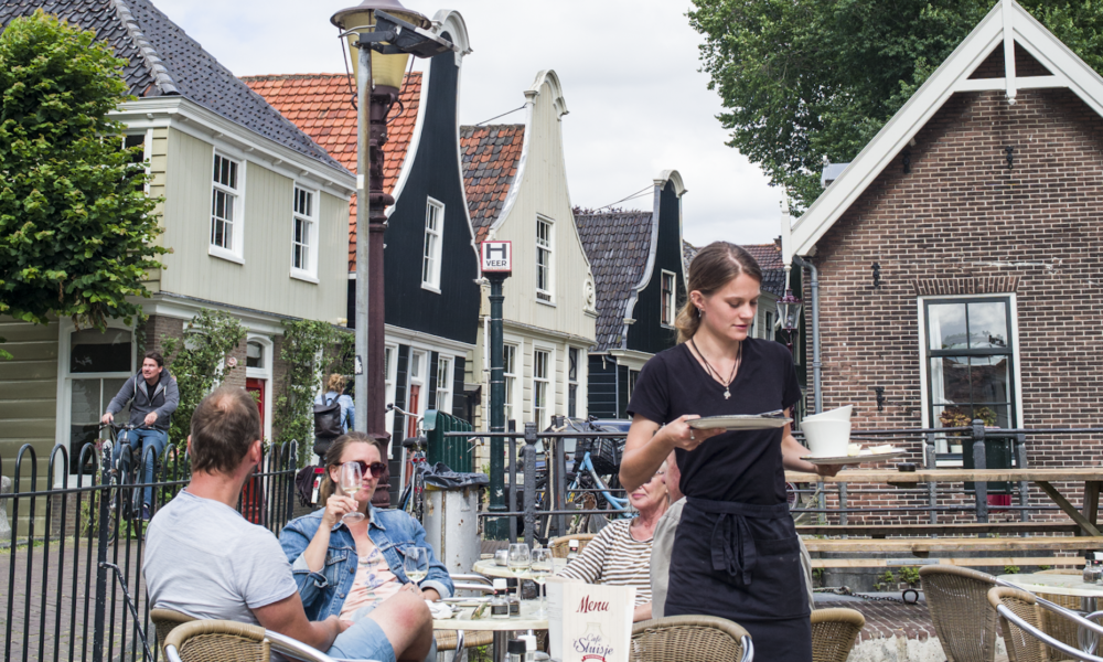 Waitress serving at a table in a quaint Dutch setting. A couple enjoys a meal in a charming outdoor cafe.