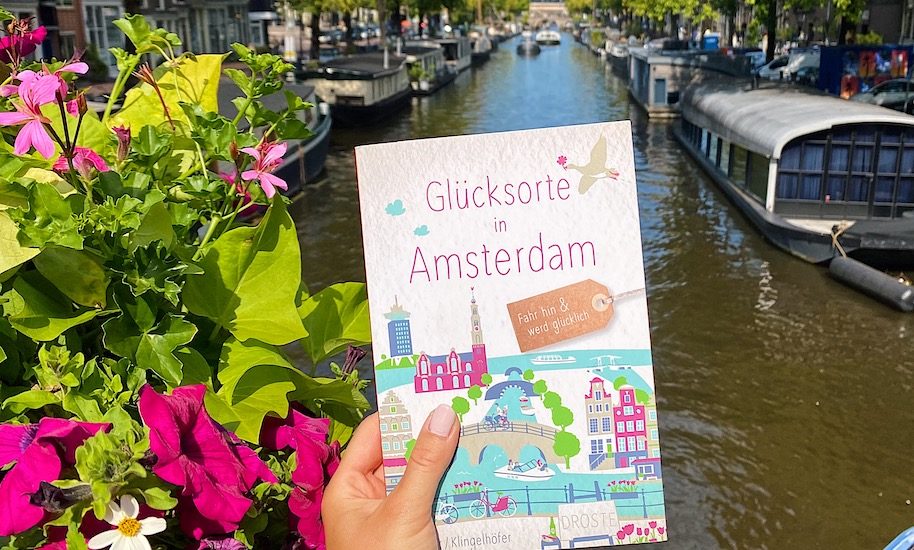 Glücksortebuch Amsterdam vor einer blumigen Gracht