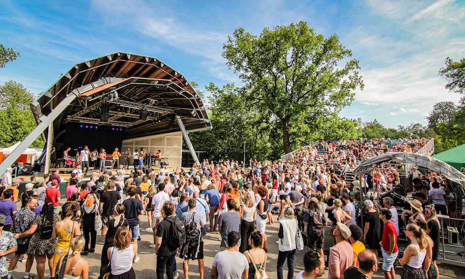 De nombreuses personnes se tiennent devant la scène du théâtre Openlucht du Vondelpark d'Amsterdam.