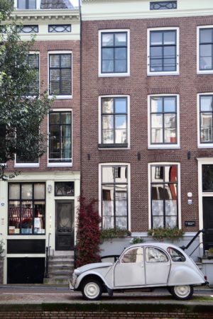 Weißer Oldtimer steht neben einem Grachtenhaus bei Firmenreise in Amsterdam