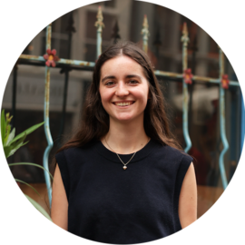 A young woman smiling at the camera. She is wearing a black top and a necklace.