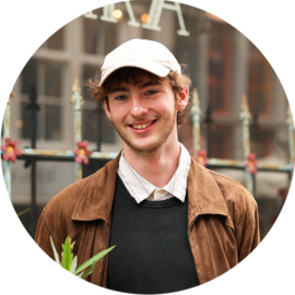 A smiling young man wearing a white cap and brown jacket