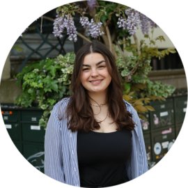 Portrait of a young woman smiling. She is standing outside.