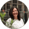 A smiling woman with dark hair standing in front of green plants. She appears to be on a city trip in Amsterdam.