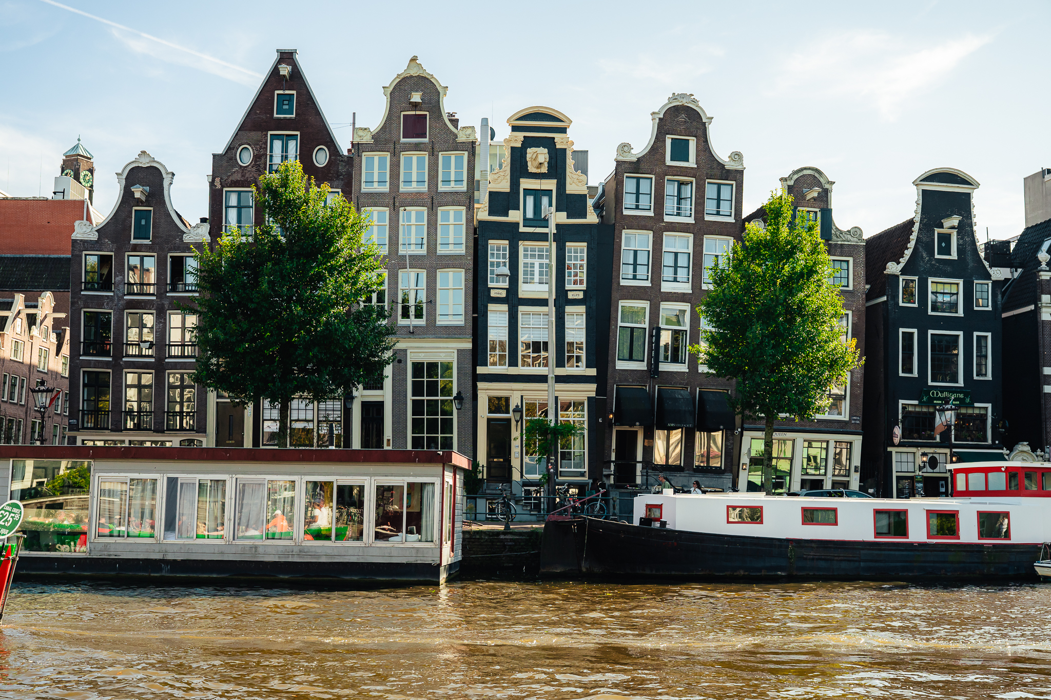 Traditional Amsterdam houses and boats on the canal. The houses are tall and narrow with ornate facades.