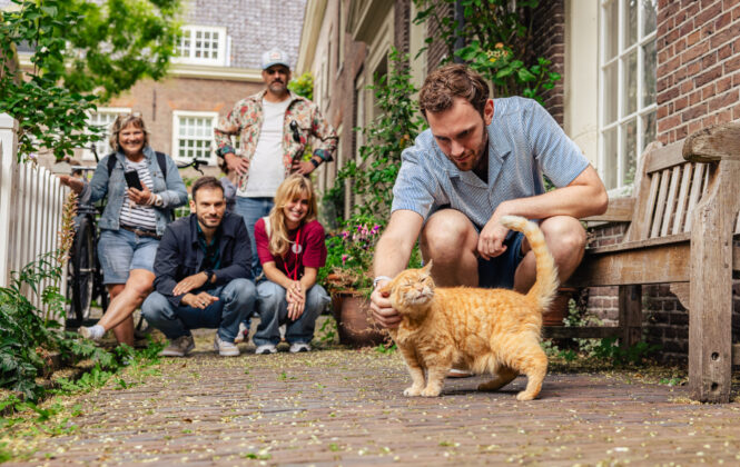 Tourist petting a cat while on a Jordaan Tour in Amsterdam. The tour group is in the Sint Andries Courtyard in Amsterdam.