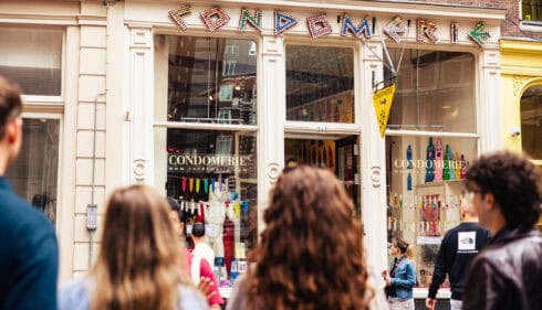 A group of tourists on a tour through the Red Light District. They are standing in front of the Condomerie, a famous shop in Amsterdam.