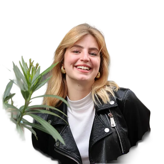 Smiling blonde woman wearing a leather jacket. She is standing next to a plant.