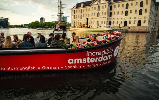 People on a boat tour in Amsterdam canal. A large building is in the background.
